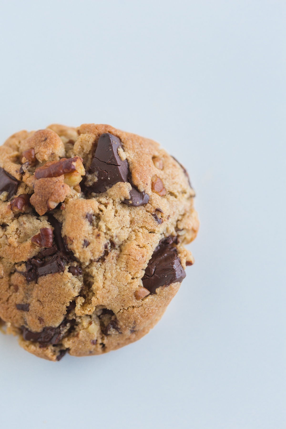A chocolate chip pecan cookie with a cracked texture and visible chocolate chips and pecan nuts.